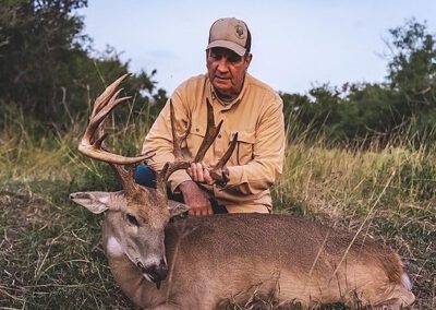 A man kneels beside a deer in a grassy field, showcasing a moment of connection with nature.